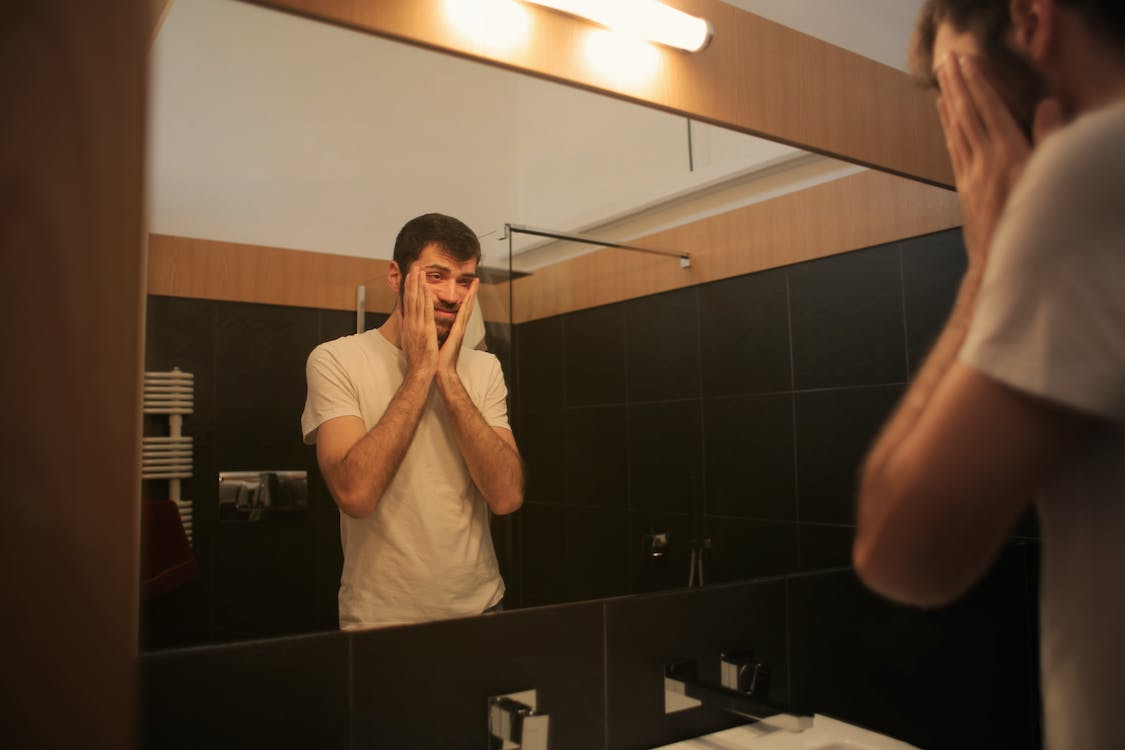 A tired person looking in the bathroom mirror