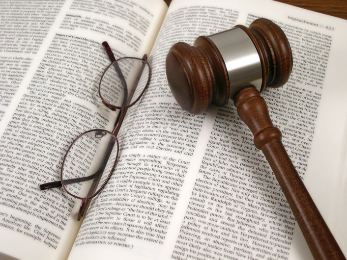 A gavel and a pair of glasses laid out on a law book.