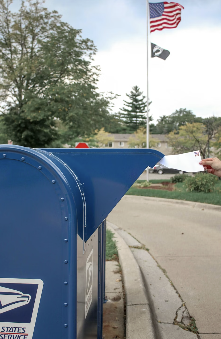 This photo shows a hand placing an envelope into a mail box.