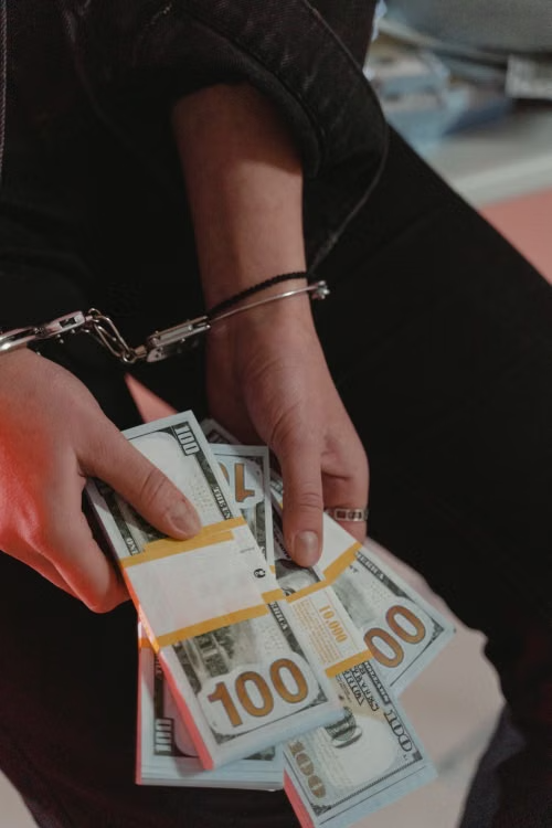  Person wearing handcuffs while holding bundles of cash for bail-related expenses